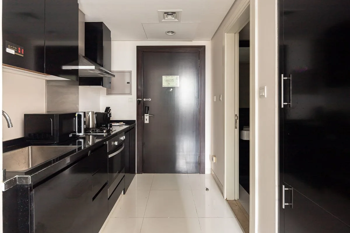 Una cocina compacta con gabinetes oscuros da a un pasillo embaldosado.