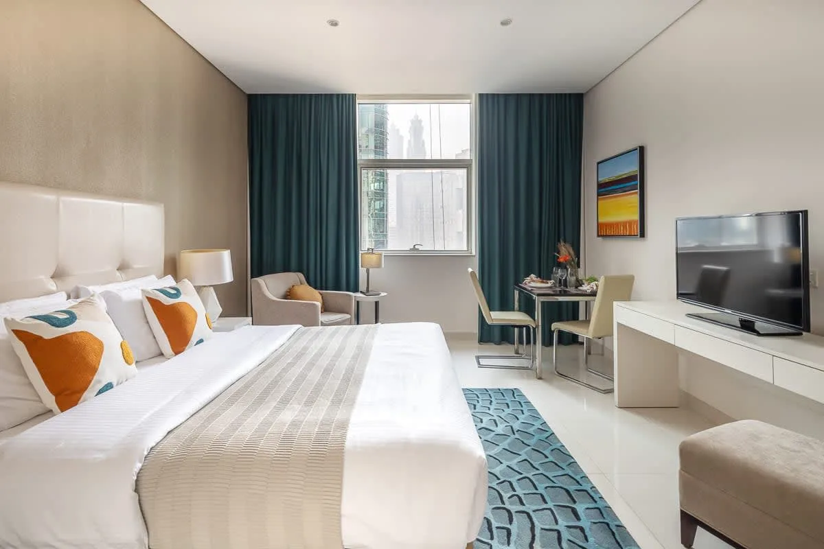 Un dormitorio con cama, zona de estar y una pequeña mesa de comedor junto a la ventana.