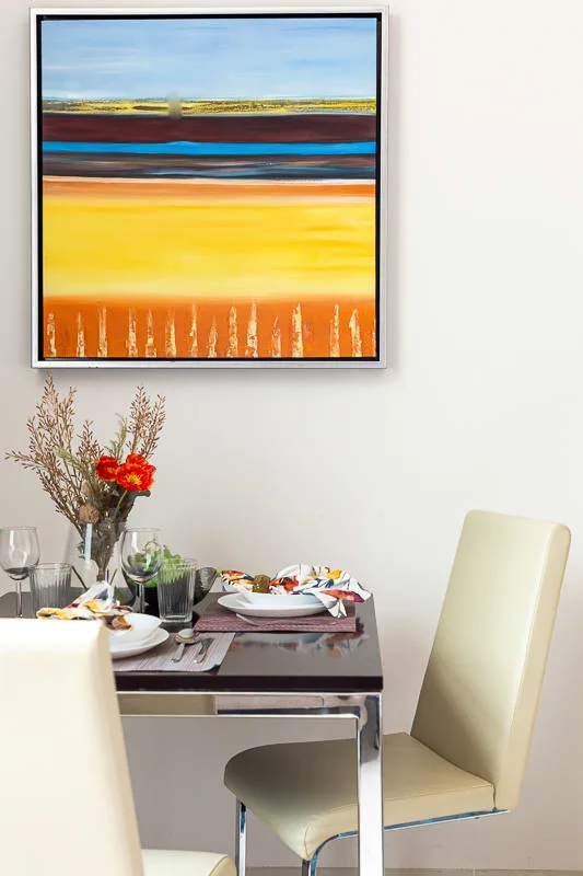 Un comedor con una mesa puesta debajo de una pintura abstracta colorida.