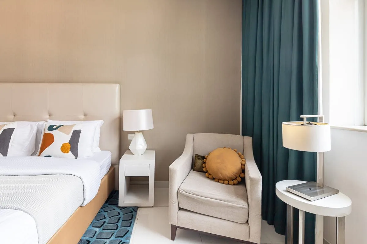 Un dormitorio con una cama junto a un sillón tapizado y una ventana.