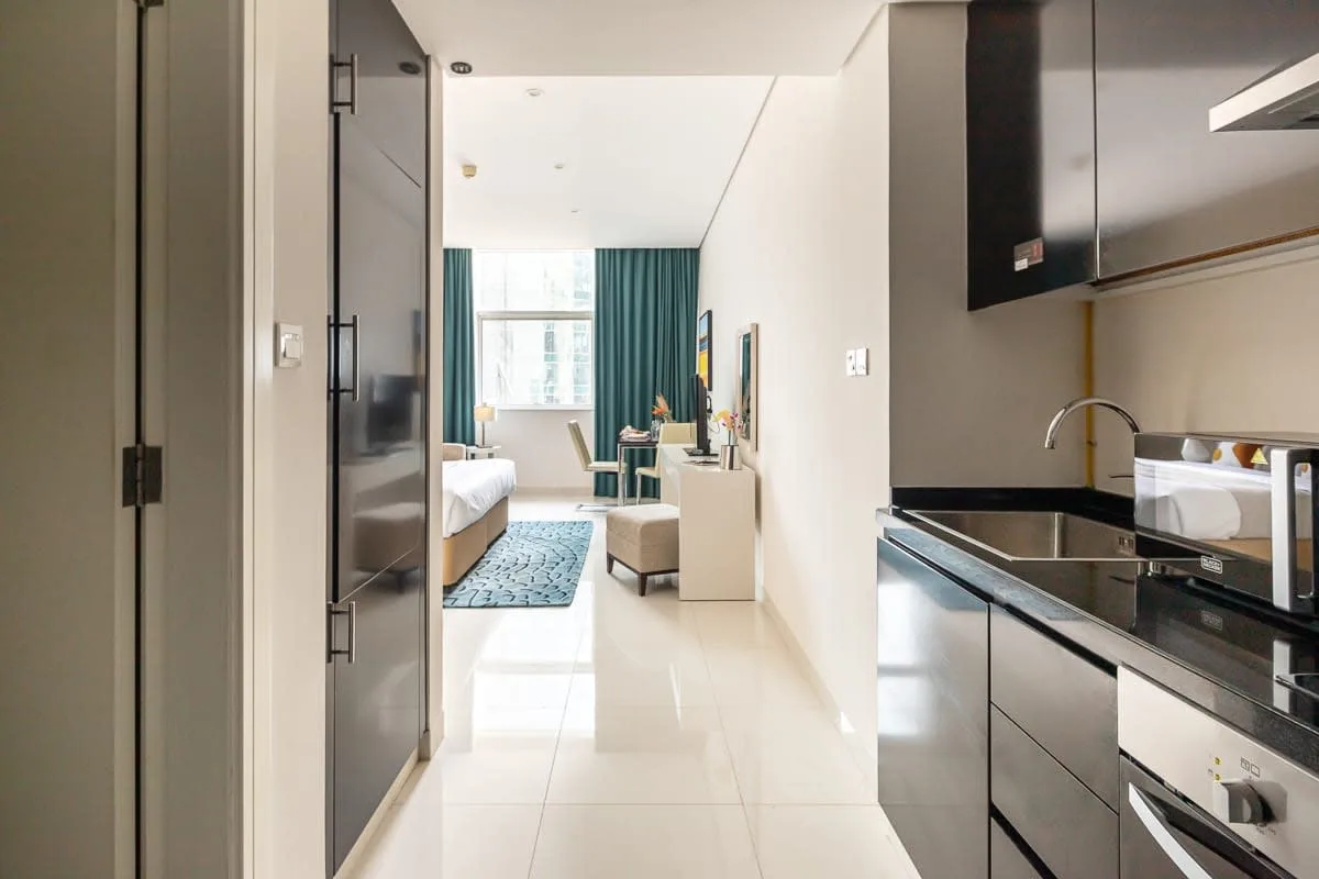 Un estudio luminoso con una pequeña cocina y una zona de estar junto a la ventana.