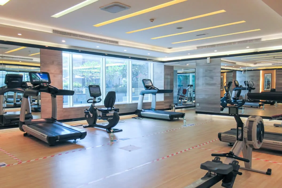 Un gimnasio con máquinas de ejercicio y grandes ventanas.