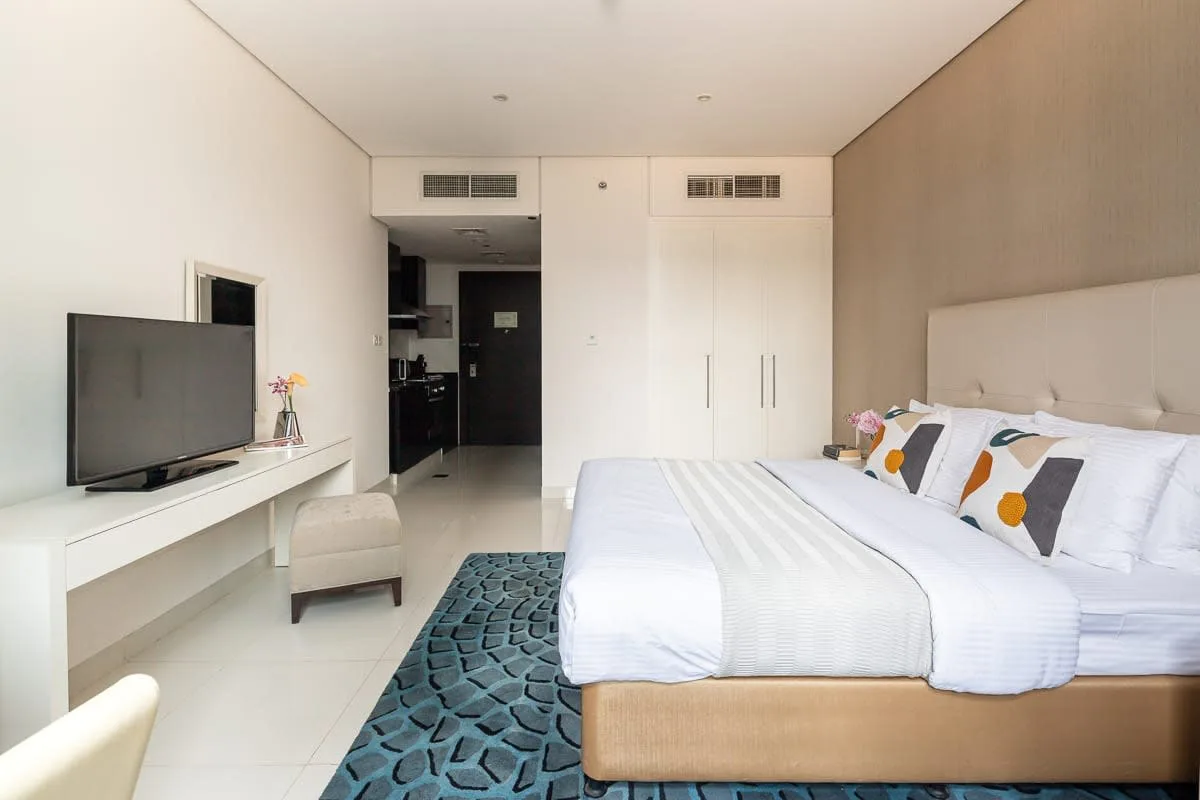 Un dormitorio con una cama grande, un televisor y una alfombra azul estampada.