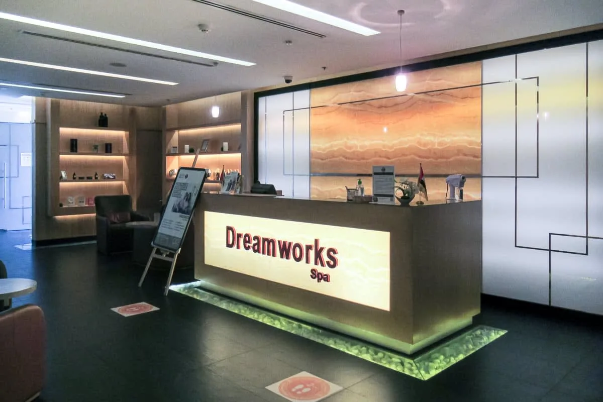 Un mostrador de recepción de spa está frente a paneles iluminados y estantes de exhibición.