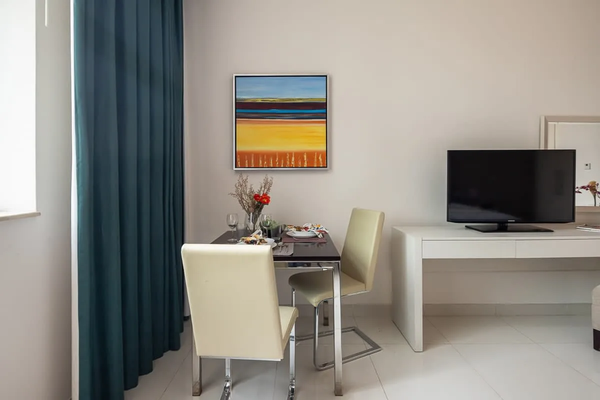 Comedor con una mesa, sillas y un televisor sobre un mueble blanco.