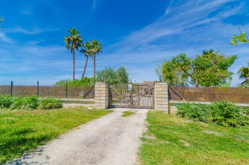 A gated entrance opens onto a gravel path bordered by grass and trees.
