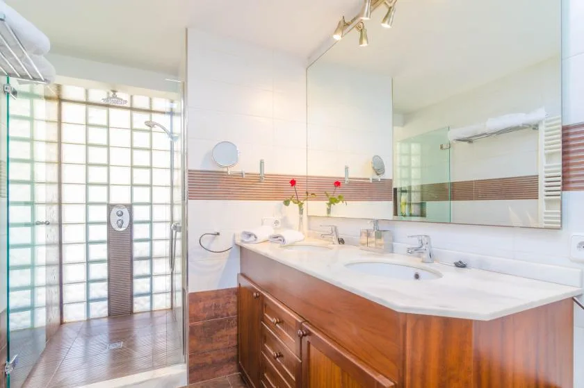 A bright bathroom with a long vanity and a glass shower area.