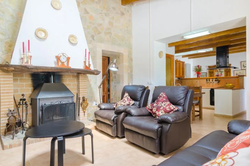 A living room with leather seating and a fireplace, opening onto a kitchen.