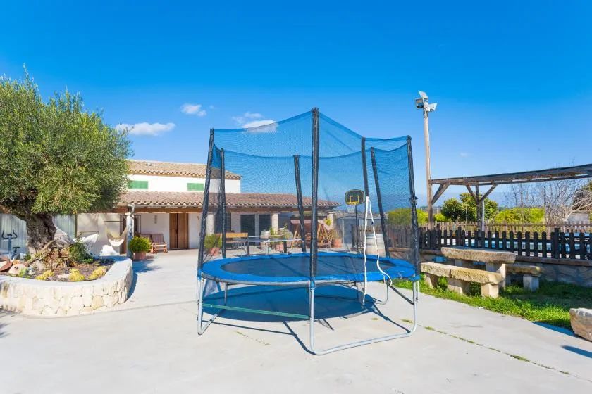 A trampoline stands in a paved outdoor courtyard beside a landscaped garden.