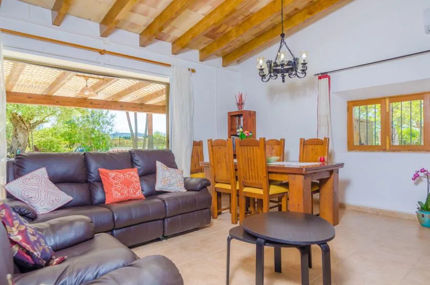 A living and dining area with seating, a wooden dining table, and exposed ceiling beams.