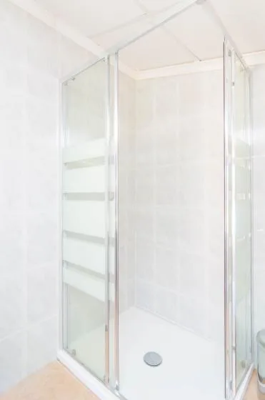 A bright bathroom shower with glass panels and a round drain.