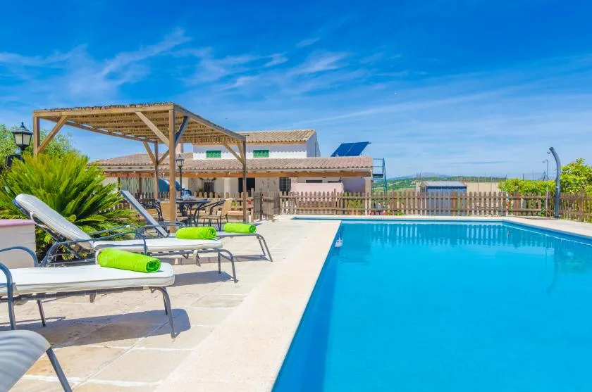 An outdoor swimming pool beside loungers and a shaded wooden pergola.