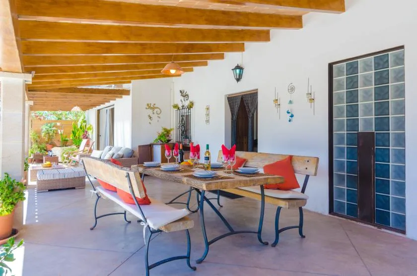 A covered outdoor dining area with a long table and seating beneath wooden beams.