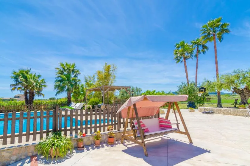 A sunny outdoor pool area with a wooden swing beneath a pink canopy.
