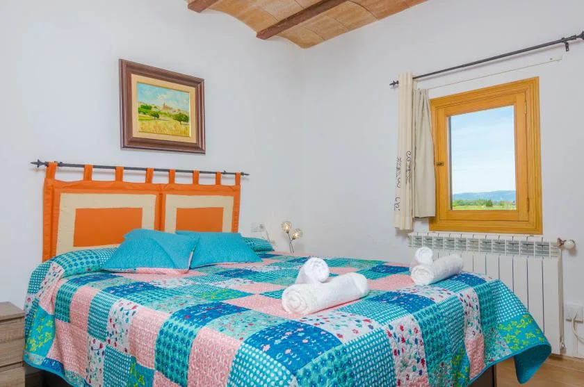 A bedroom with a colorful bed beneath a framed landscape painting.