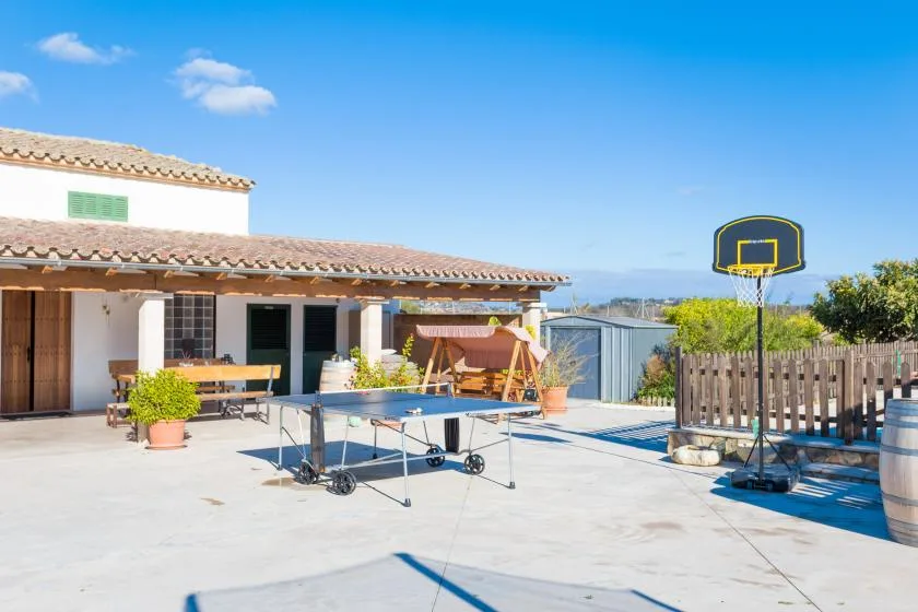 A sunny outdoor patio with a table tennis table, basketball hoop, and seating.