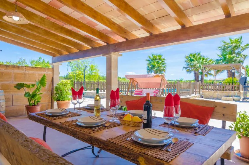 A covered outdoor dining area with a table set beneath a wooden-beam roof.