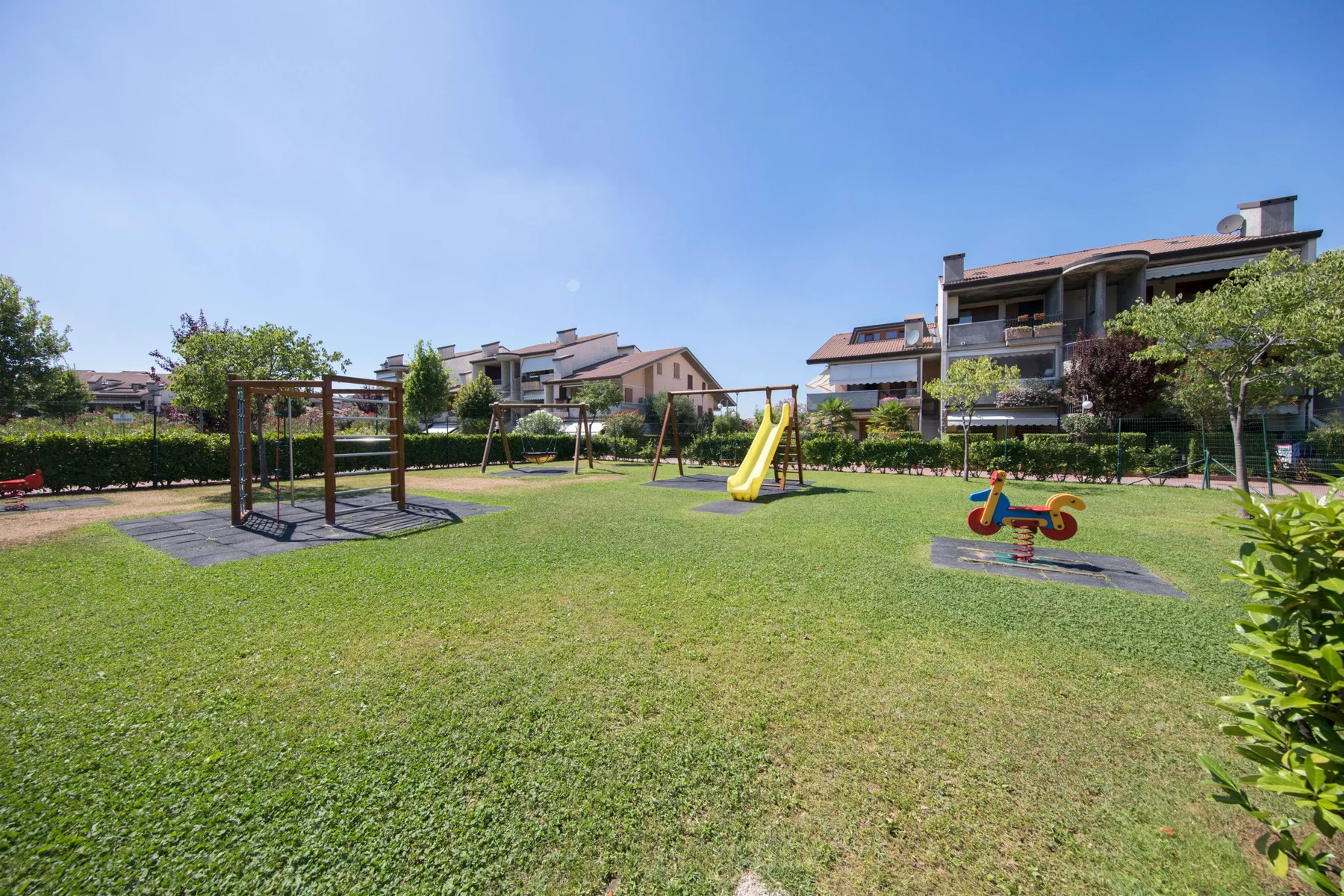 A grassy outdoor playground with a swing set and yellow slide.