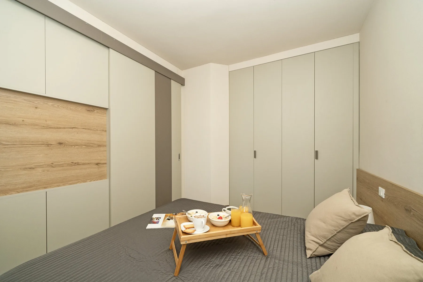 A bedroom with a low bed, pale cabinetry, and a small serving tray.