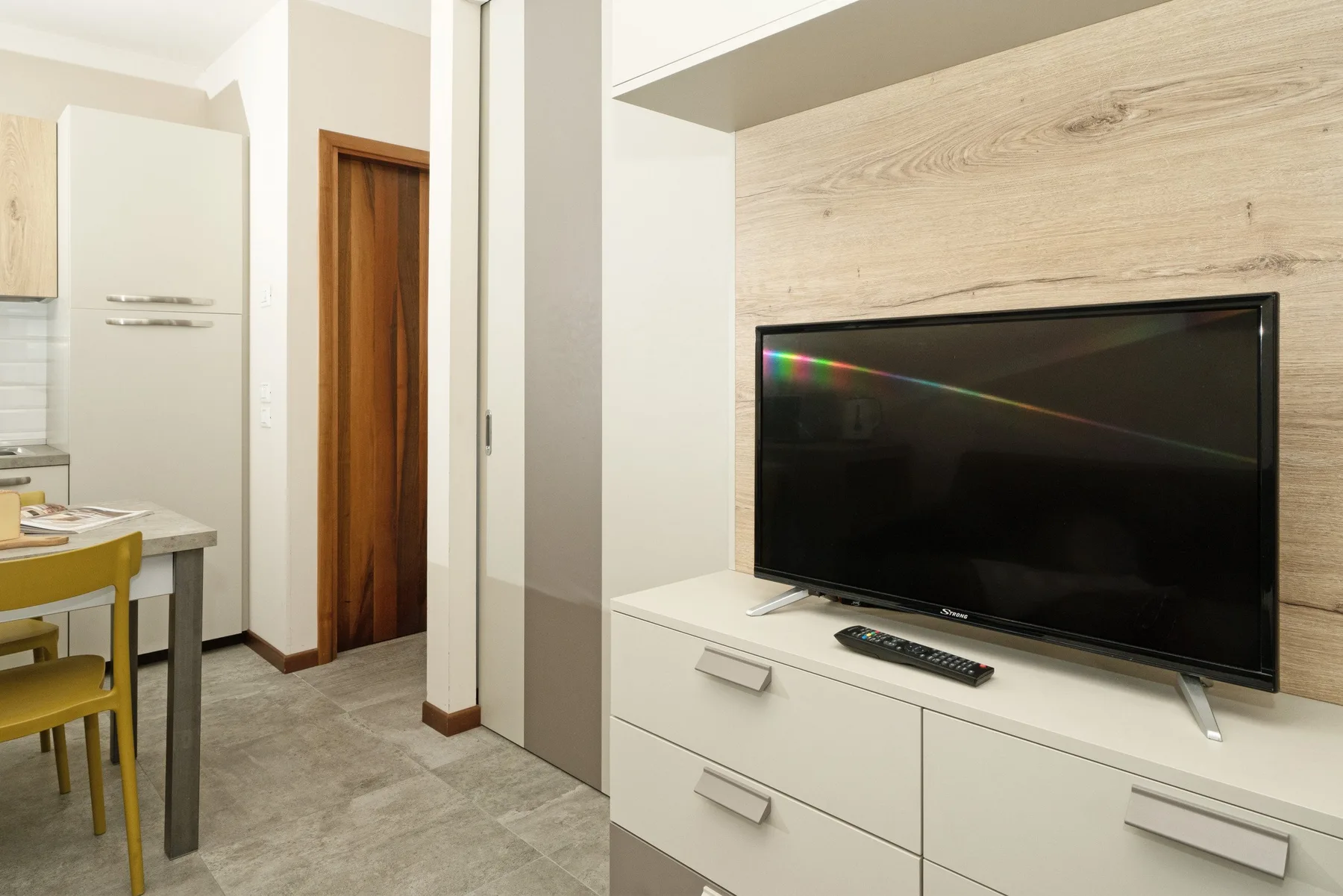 A living area with a television on a cabinet beside a small dining space.