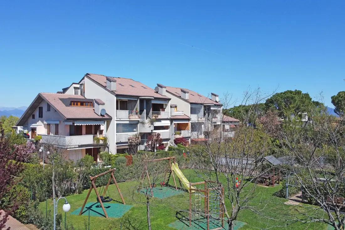 A row of residential buildings overlooks a landscaped garden with playground equipment.