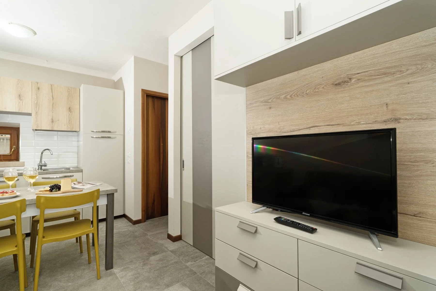 A dining area beside a television cabinet, with a table and yellow chairs.