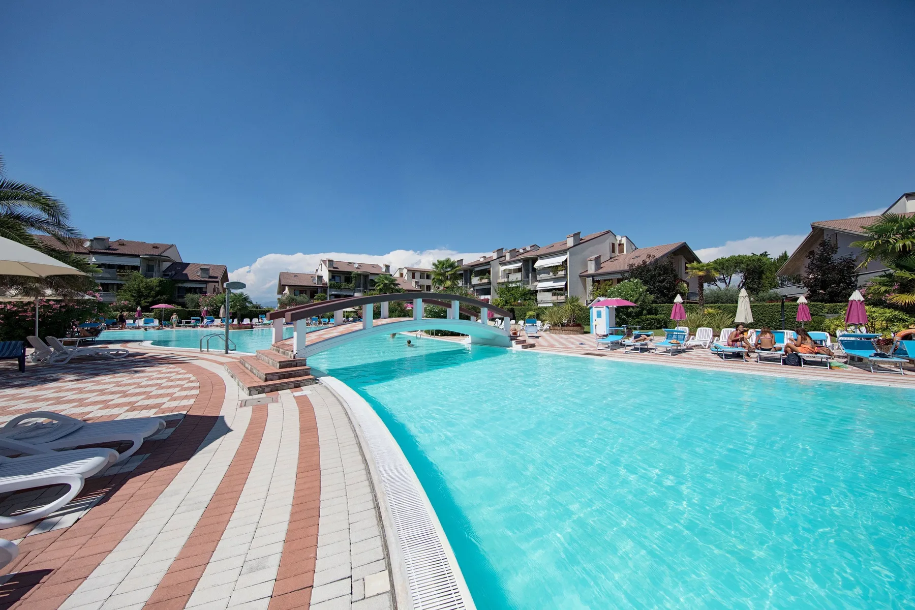 An outdoor swimming pool with a small arched footbridge and surrounding lounge chairs.