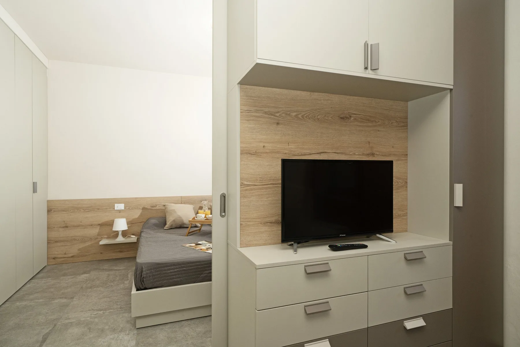 A bedroom with a bed beside a built-in cabinet and television.
