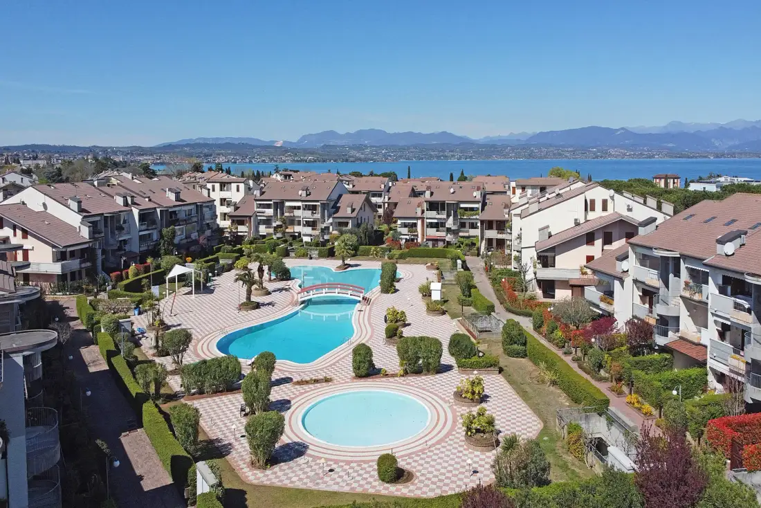Aerial view of a residential complex with swimming pools and a lake beyond.