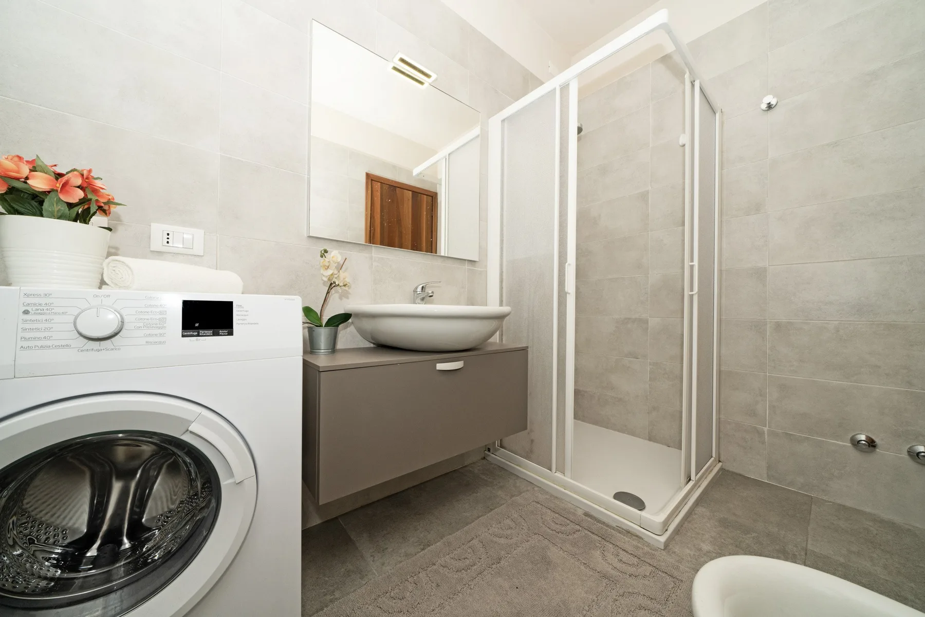 A bathroom with a shower, sink, and washing machine.