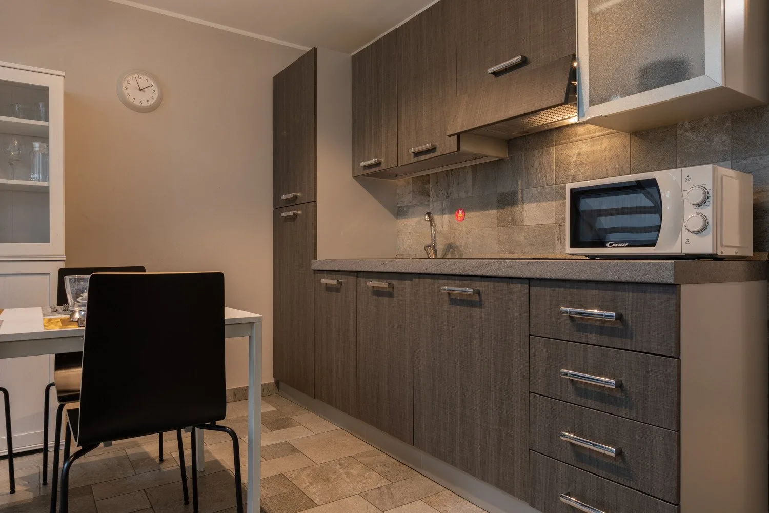 A kitchen with dark cabinets, a countertop, and a microwave beside a dining table.