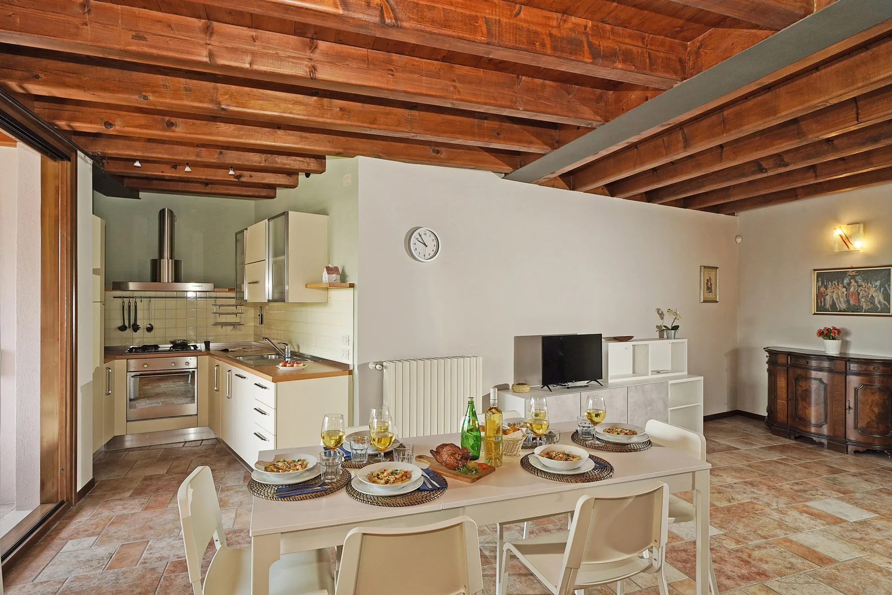 Comedor de planta abierta con cocina y mesa puesta bajo vigas de madera a la vista.