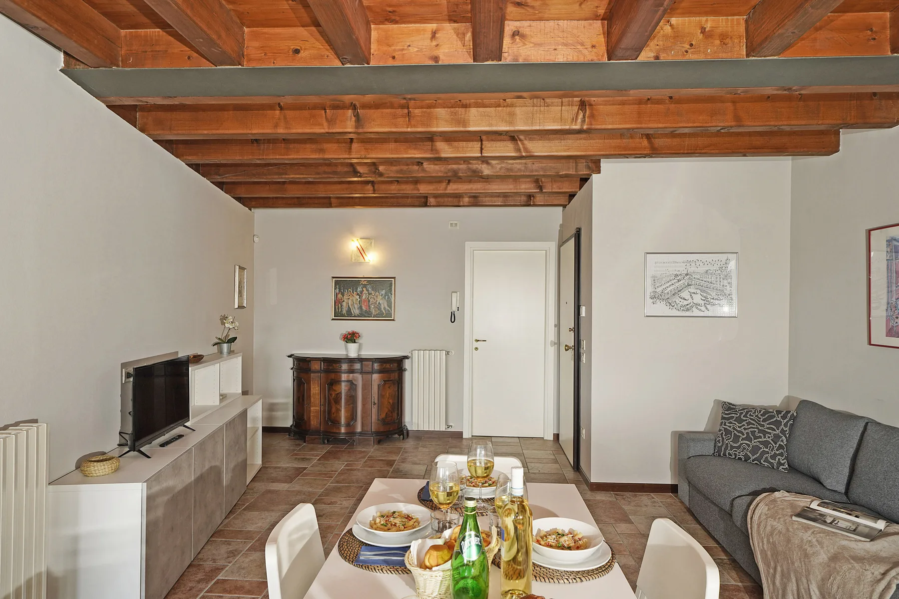 Una sala de estar con mesa de comedor, asientos grises y vigas de madera expuestas en el techo.