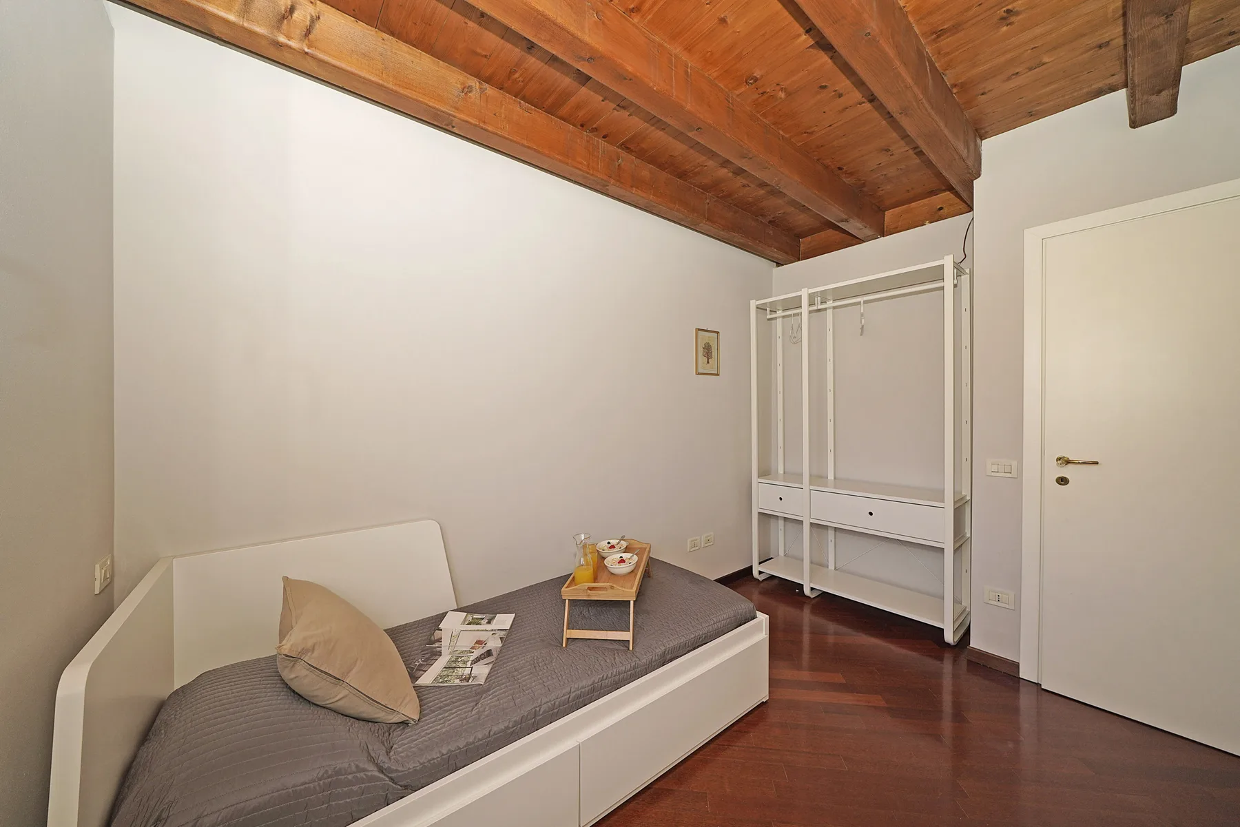 Un dormitorio compacto con una cama individual bajo un techo de madera inclinado.