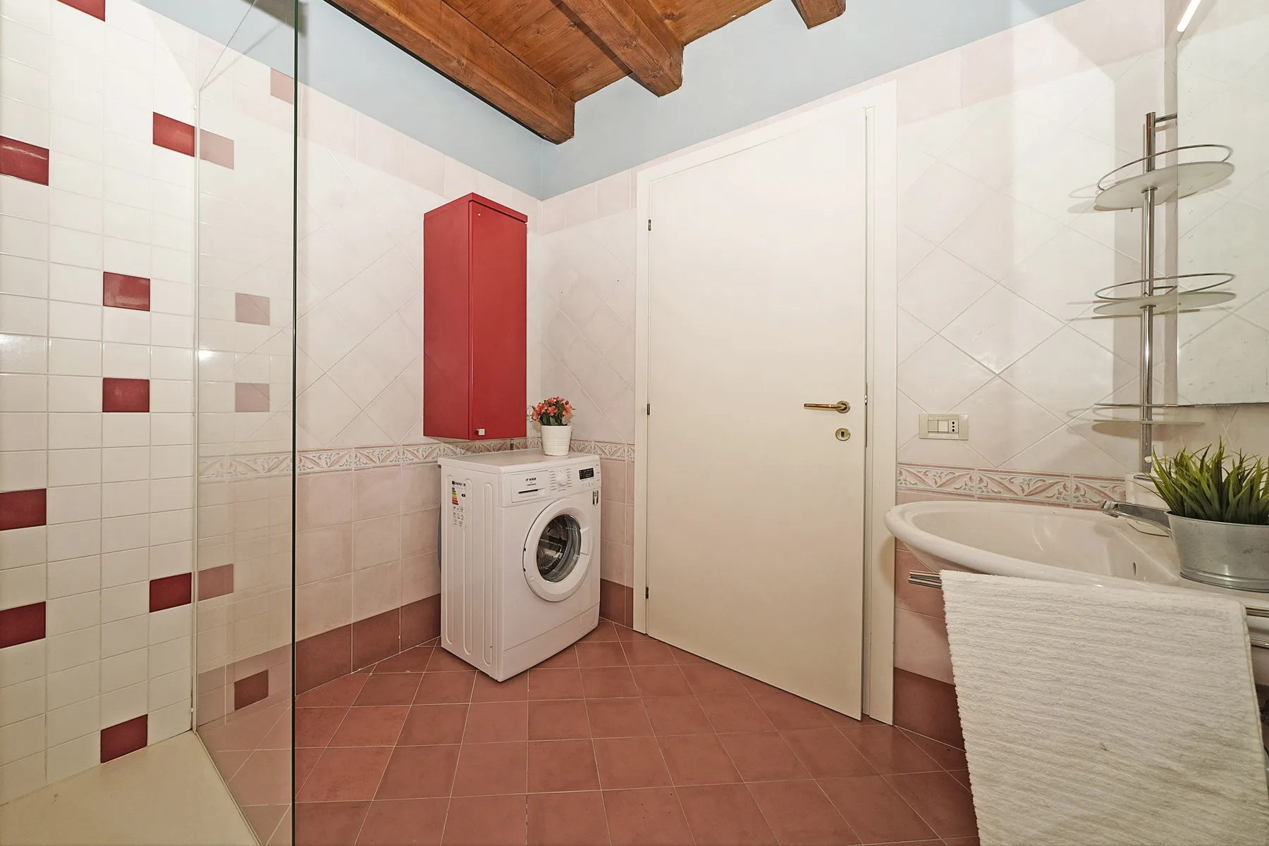 Un baño alicatado con lavadora, bañera y mampara de ducha de vidrio.