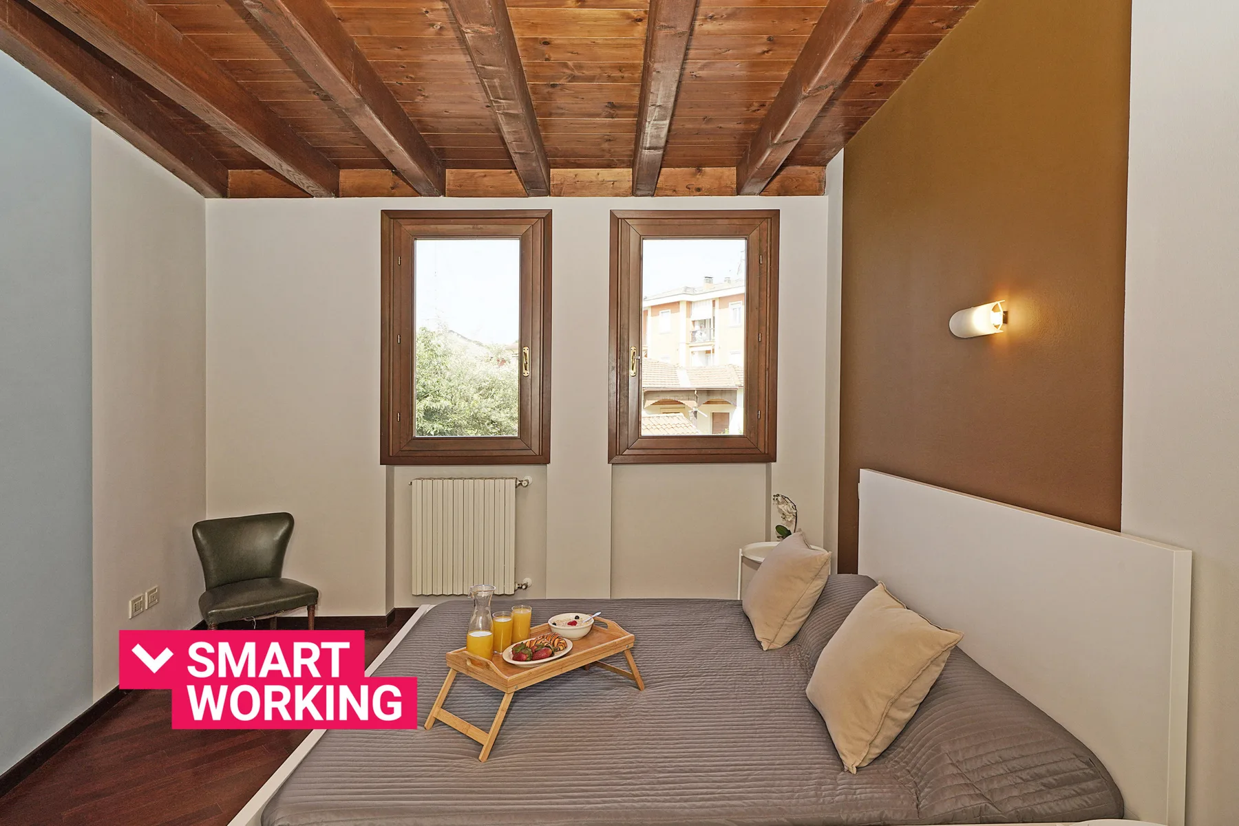Un dormitorio con una cama, dos ventanas y vigas de madera a la vista.
