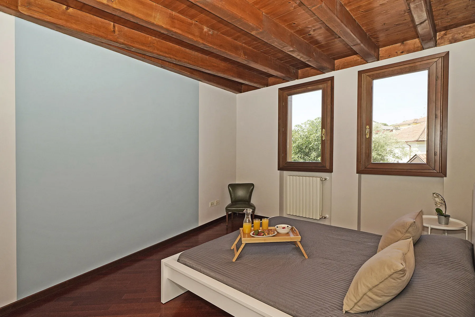 Un dormitorio con una cama baja, dos ventanas y un techo de madera.