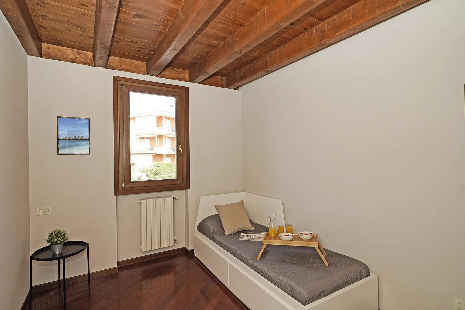 Un dormitorio sencillo con una cama individual, una ventana y vigas de madera a la vista en el techo.