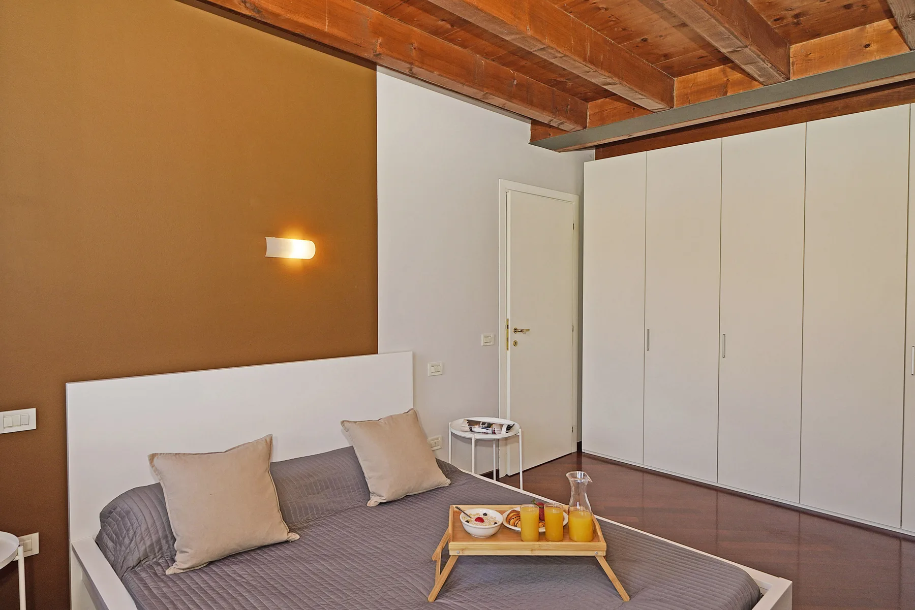 Un dormitorio con una cama, una mesa pequeña y armarios empotrados bajo un techo de madera.