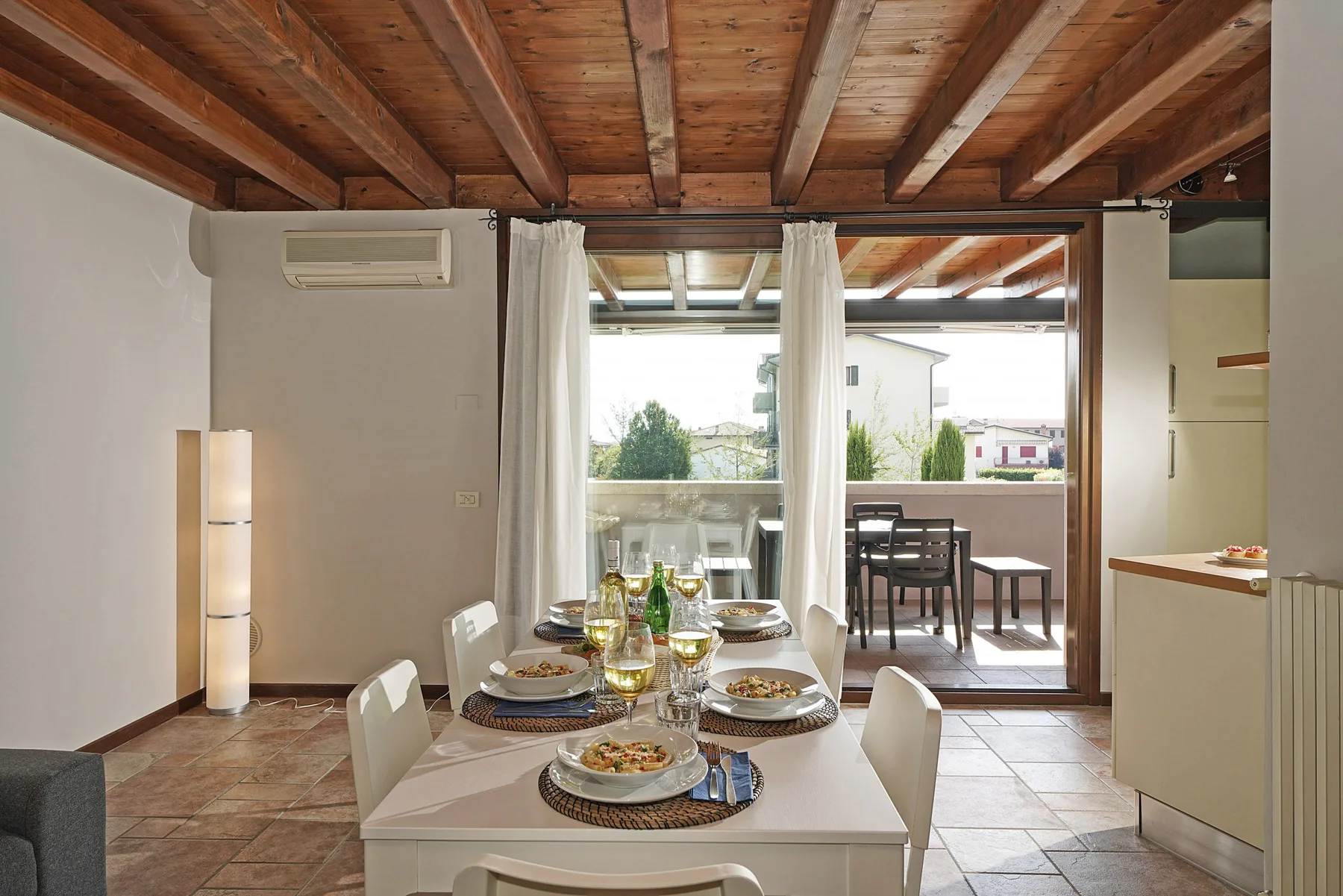 Comedor con la mesa puesta junto a amplias puertas de vidrio que dan a un patio.