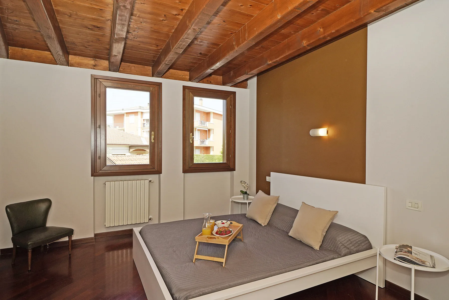 Un dormitorio con una cama bajo dos ventanas y vigas de madera a la vista.