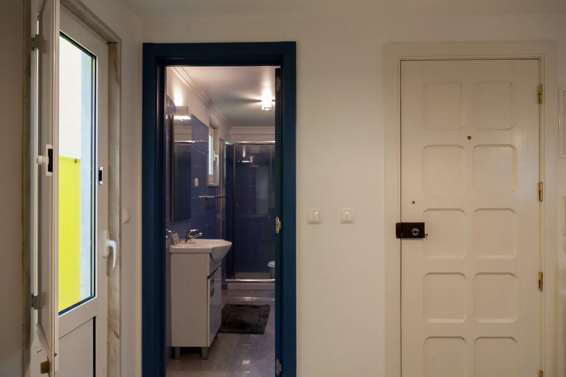 Un pasillo con una puerta blanca y una entrada abierta a un baño.
