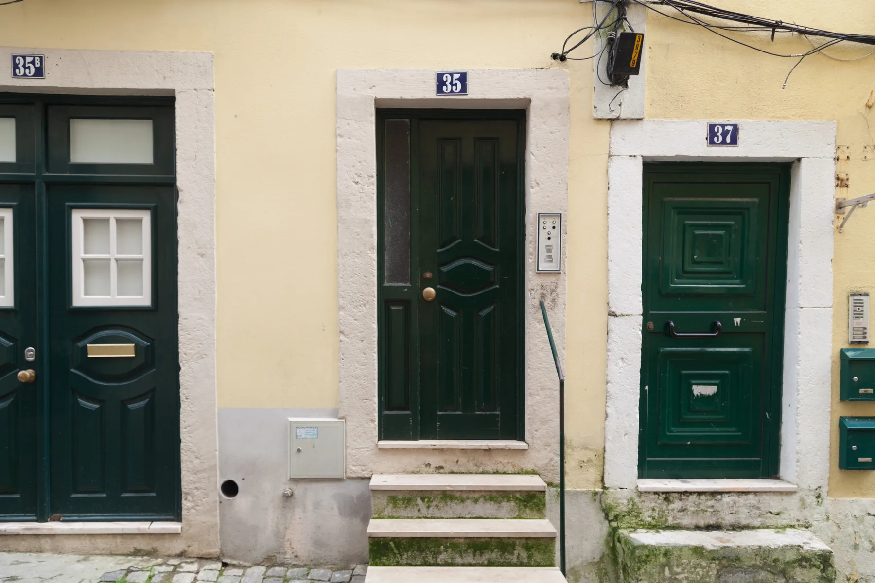 Una fila de puertas verdes oscuras en la fachada de un edificio amarillo pálido.