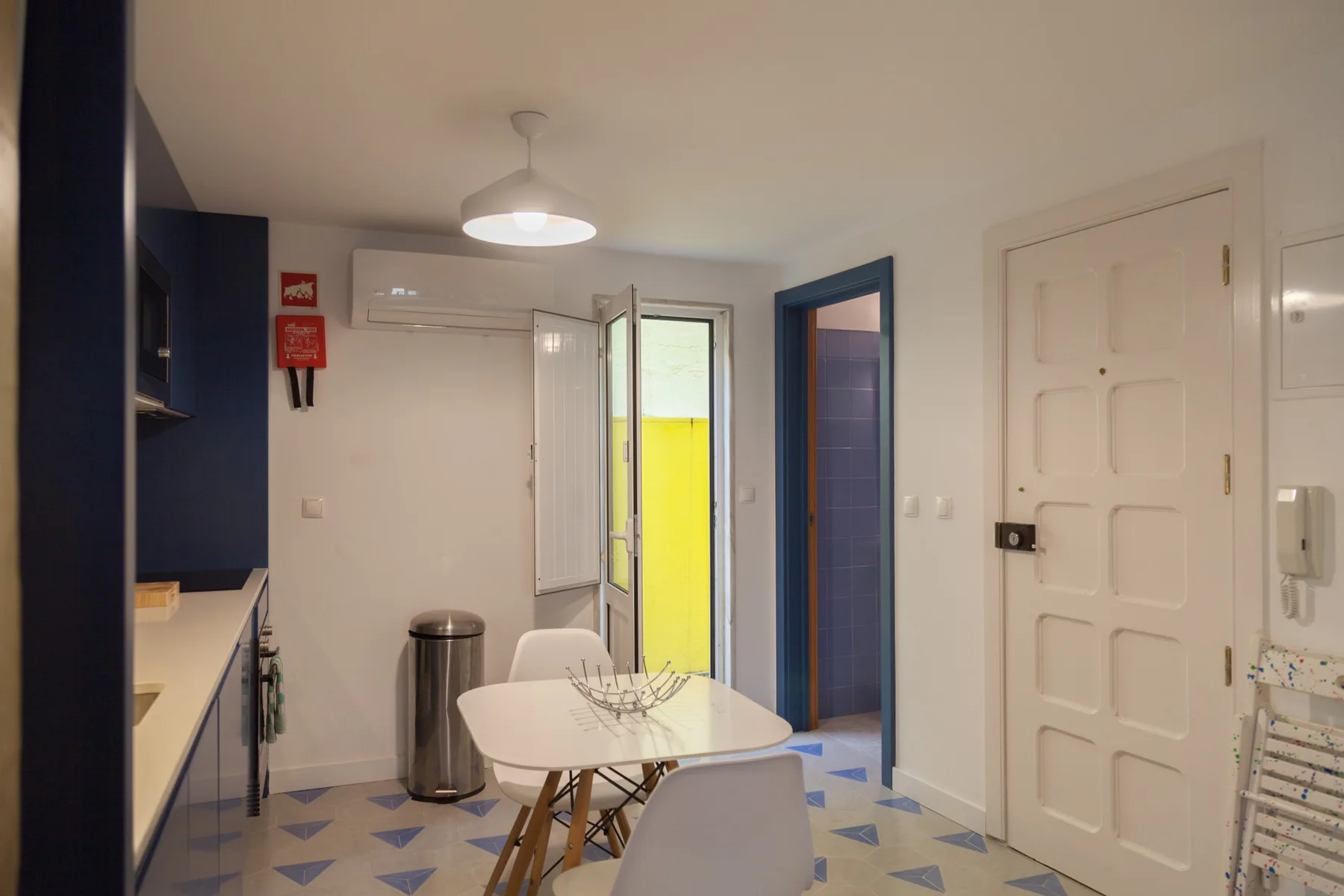 Un comedor con mesa y asientos junto a una pequeña cocina.