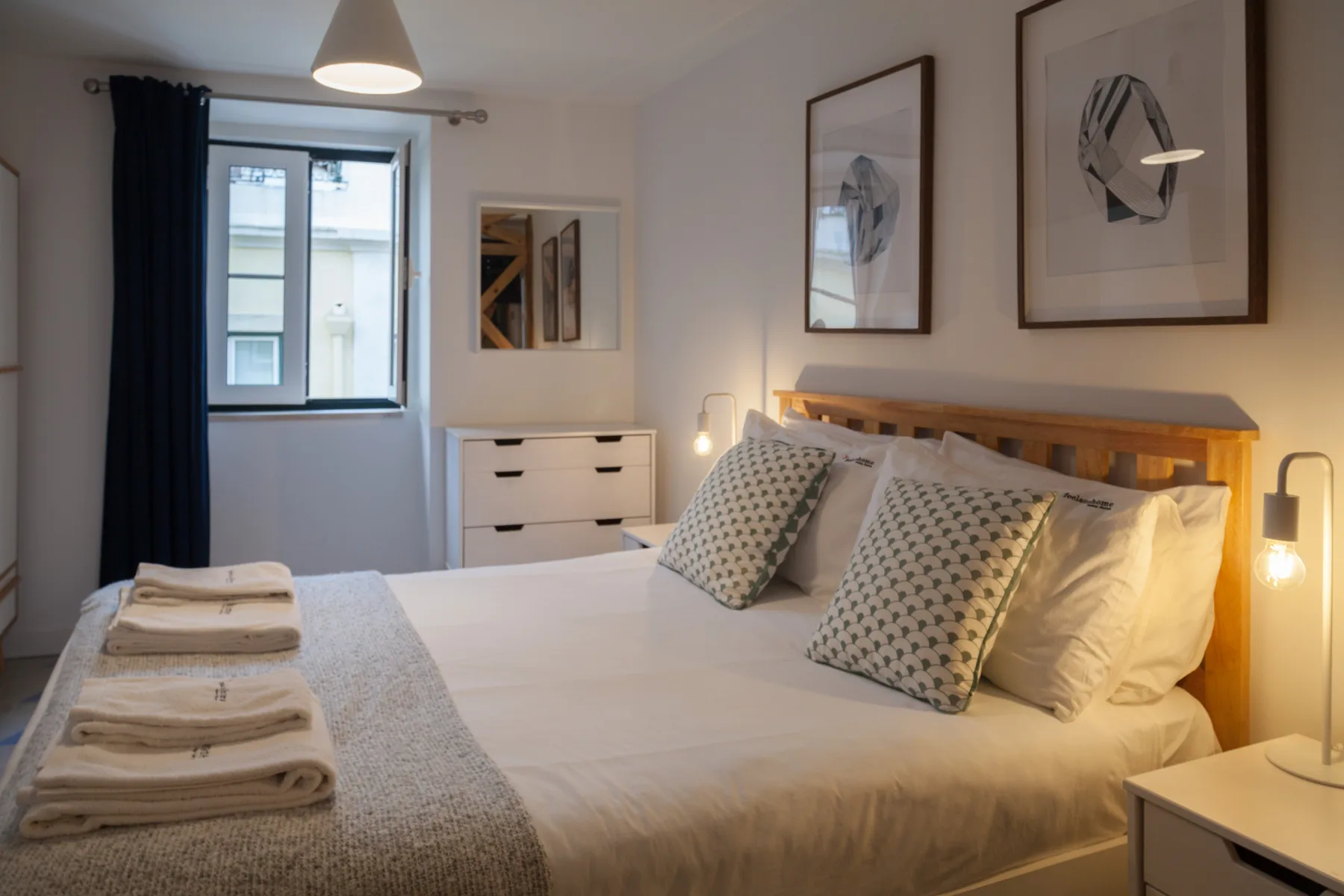 Un dormitorio con una cama bien hecha, lámparas de noche y cuadros enmarcados.