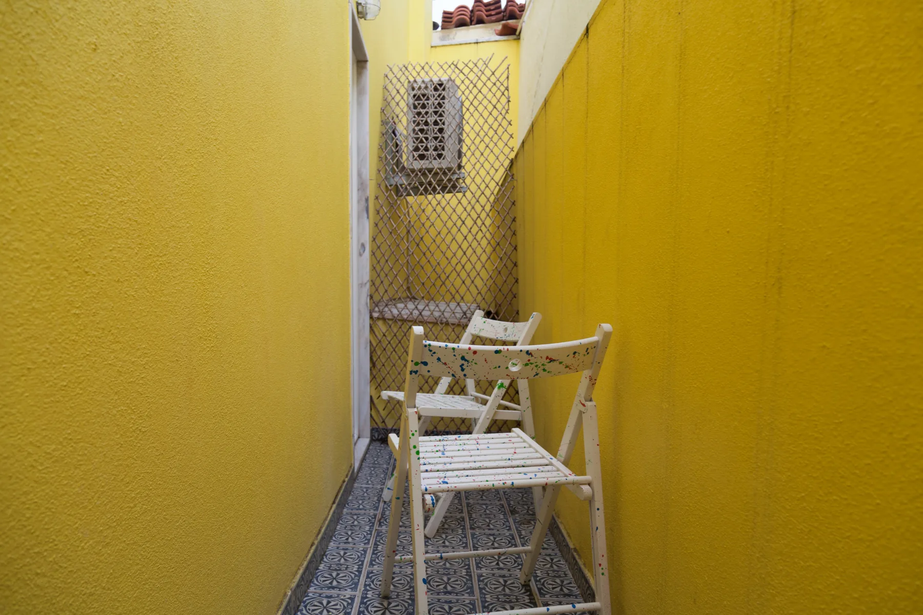 Un pasillo exterior estrecho con paredes amarillas y asientos plegables.