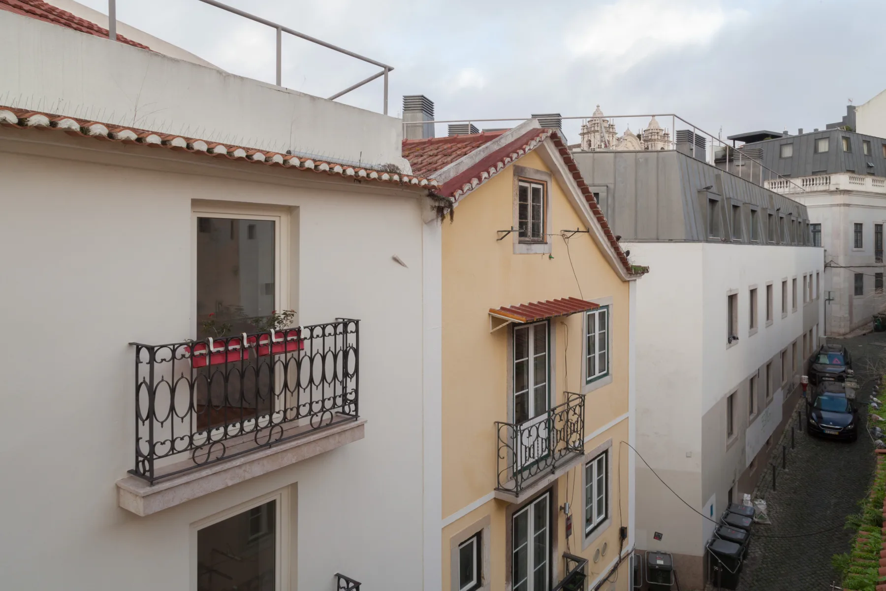 Vista de una calle con edificios próximos, balcones y tejados de tejas rojas.