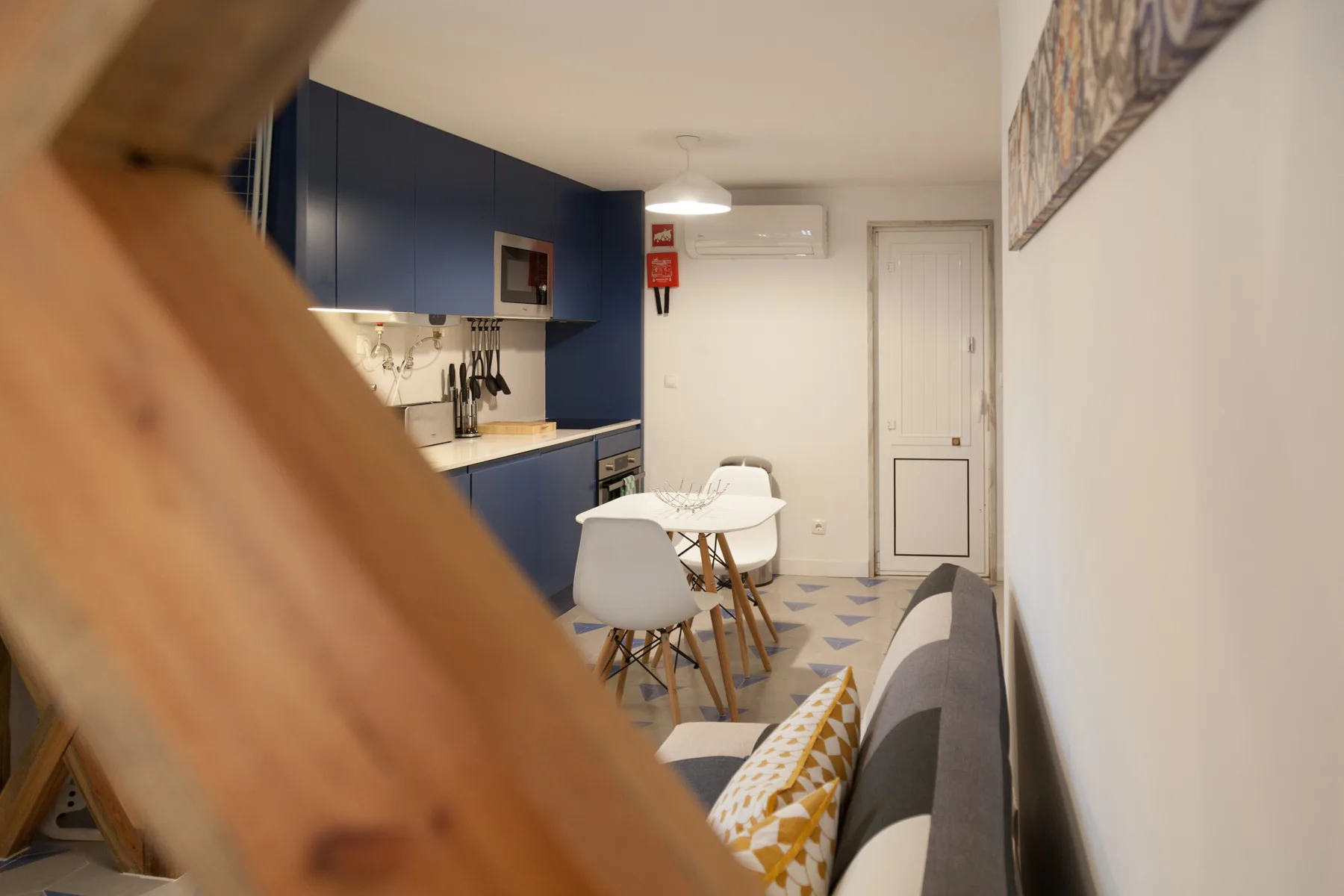 Una pequeña zona de comedor y cocina con mesa, sillas y armarios azules.