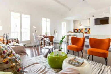 A bright living room has orange seating, a glass dining table, and large windows.