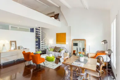 A bright living and dining area with orange seating and a wooden dining table.